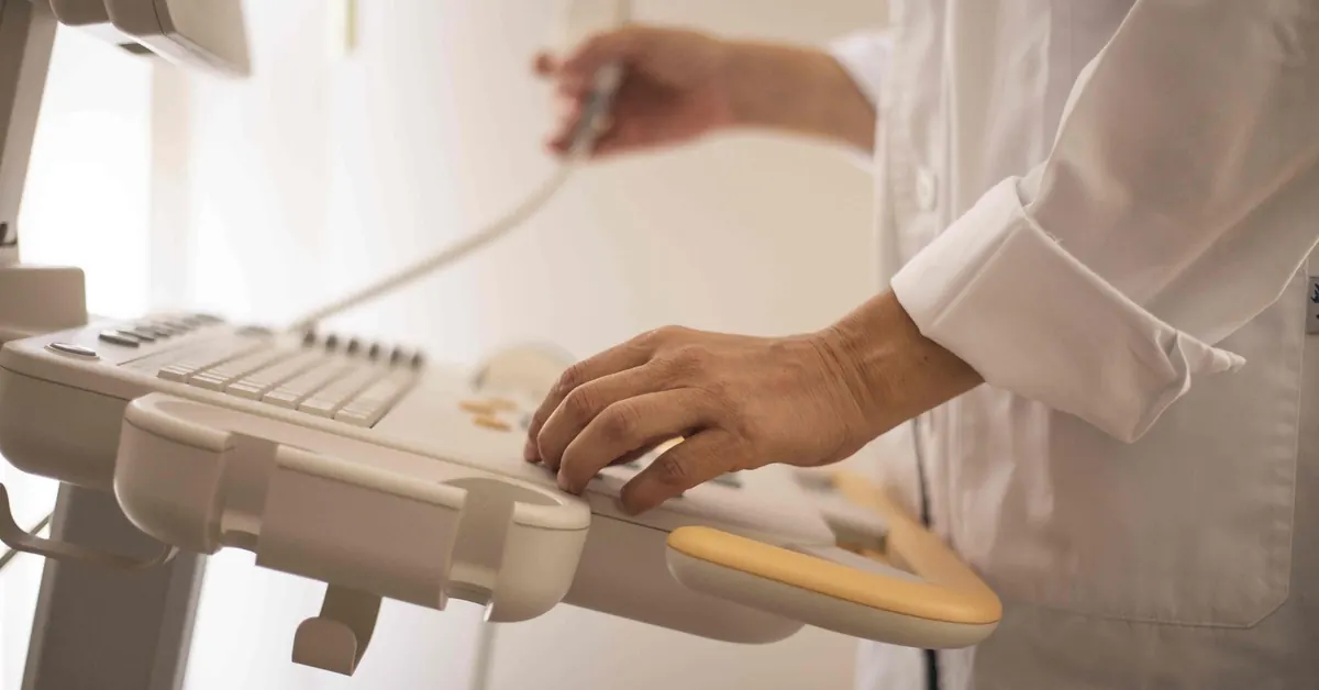 Mano de un médico sosteniendo el transductor sobre el teclado de un equipo de ultrasonido